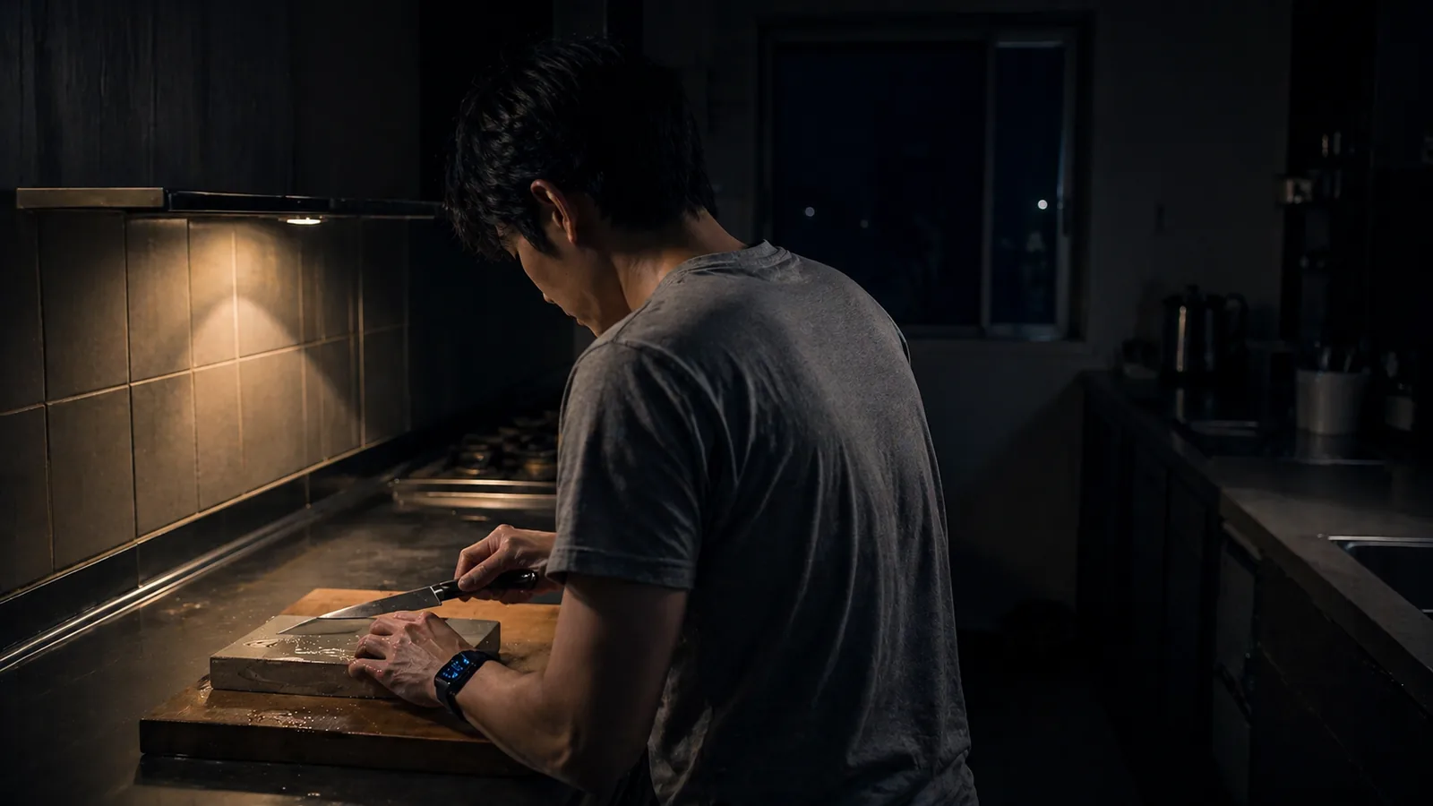 静岡の夜のキッチンで砥石を前に包丁を研ぐコウスケの後ろ姿
